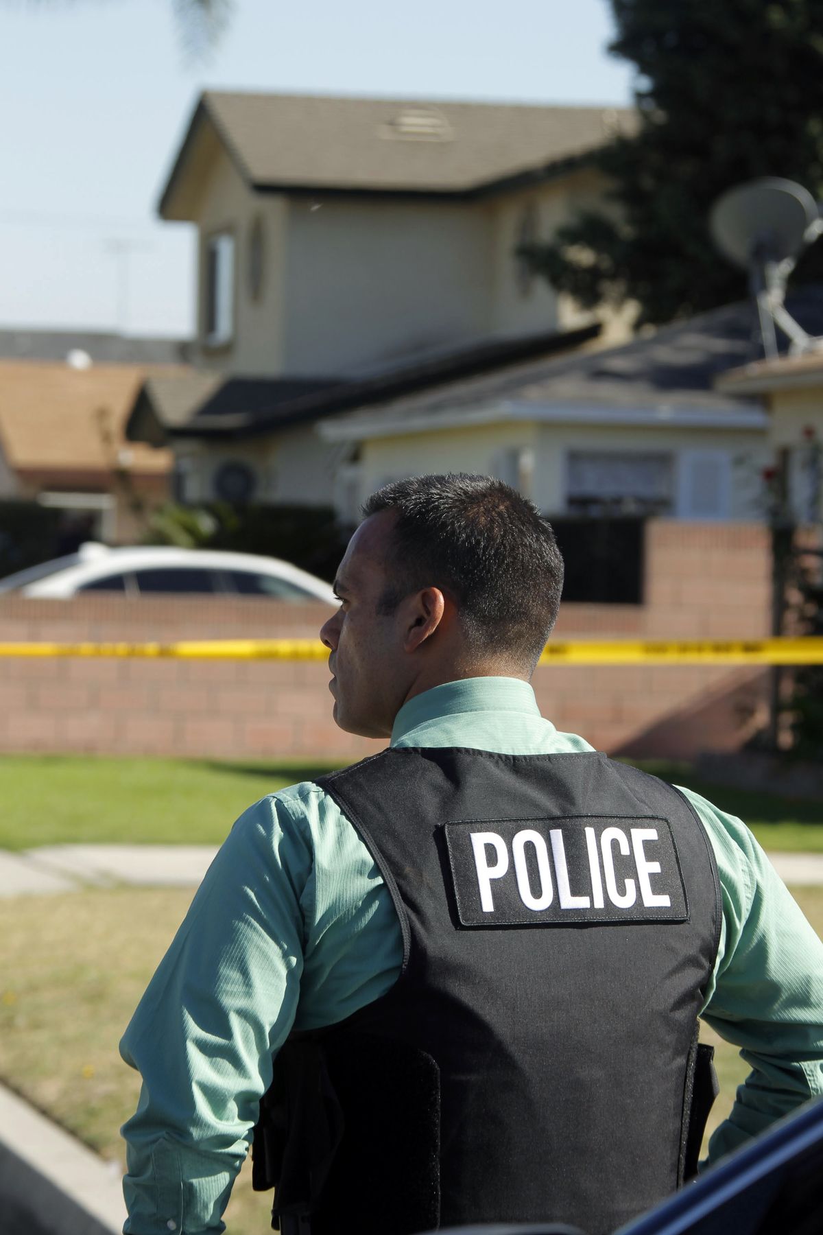 A police officer is seen down the street from the two-story home, background, where one person was found shot to death in Downey, Calif., Wednesday, Oct. 24, 2012.  Five people were shot and at least two died in shootings at a business and a residence in the Los Angeles suburb Wednesday, according to Downey police Lt. Dean Milligan.  The shootings occurred shortly after 11 a.m. at a business and at a nearby home, where family members of the business owner live. A woman was found dead at the home, he said. (Nick Ut / Associated Press)