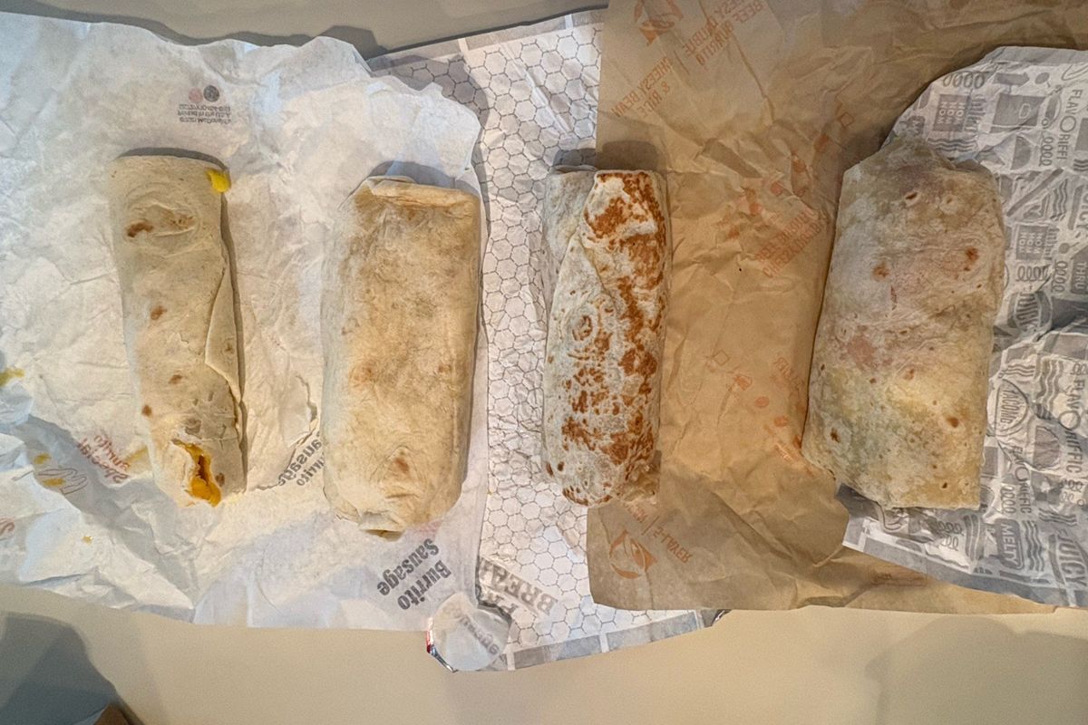Four fast-food burritos from Spokane restaurant chains are lined up to compare size and heft. (Bruce Howard/For The Spokesman-Review)