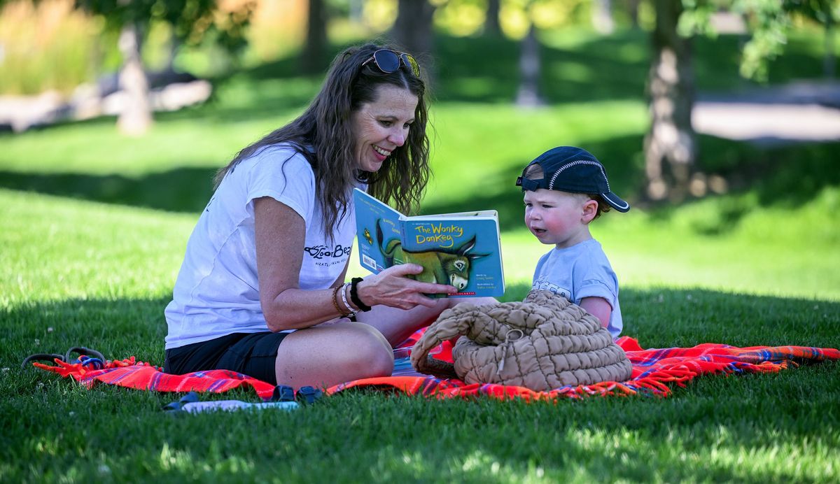 “He’s just about 2 years old,” Stephani Lind says as she reads to her grandson Bodhi Lind during their picnic lunch near Discovery Playground on Thursday in Spokane Valley.  (Kathy Plonka/The Spokesman-Review)