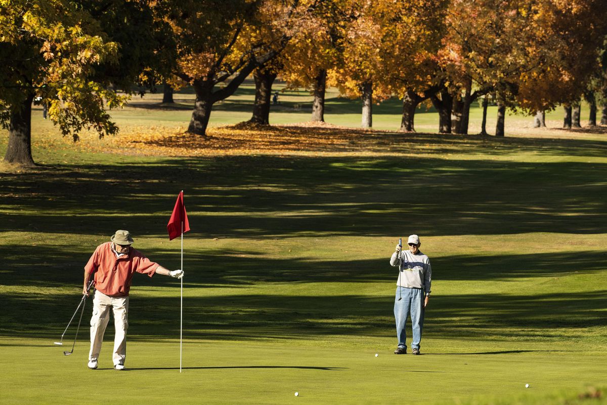 Jack Dunsmoor pulls the flag as John Fort lines up a putt on the 18th green at Esmeralda Golf Course, Monday, Oct. 22, 2018. Golfers at local courses are enjoying the warmer than normal temperatures. Barring bad weather, Esmeralda plans to stay open until mid November. (Colin Mulvany / The Spokesman-Review)