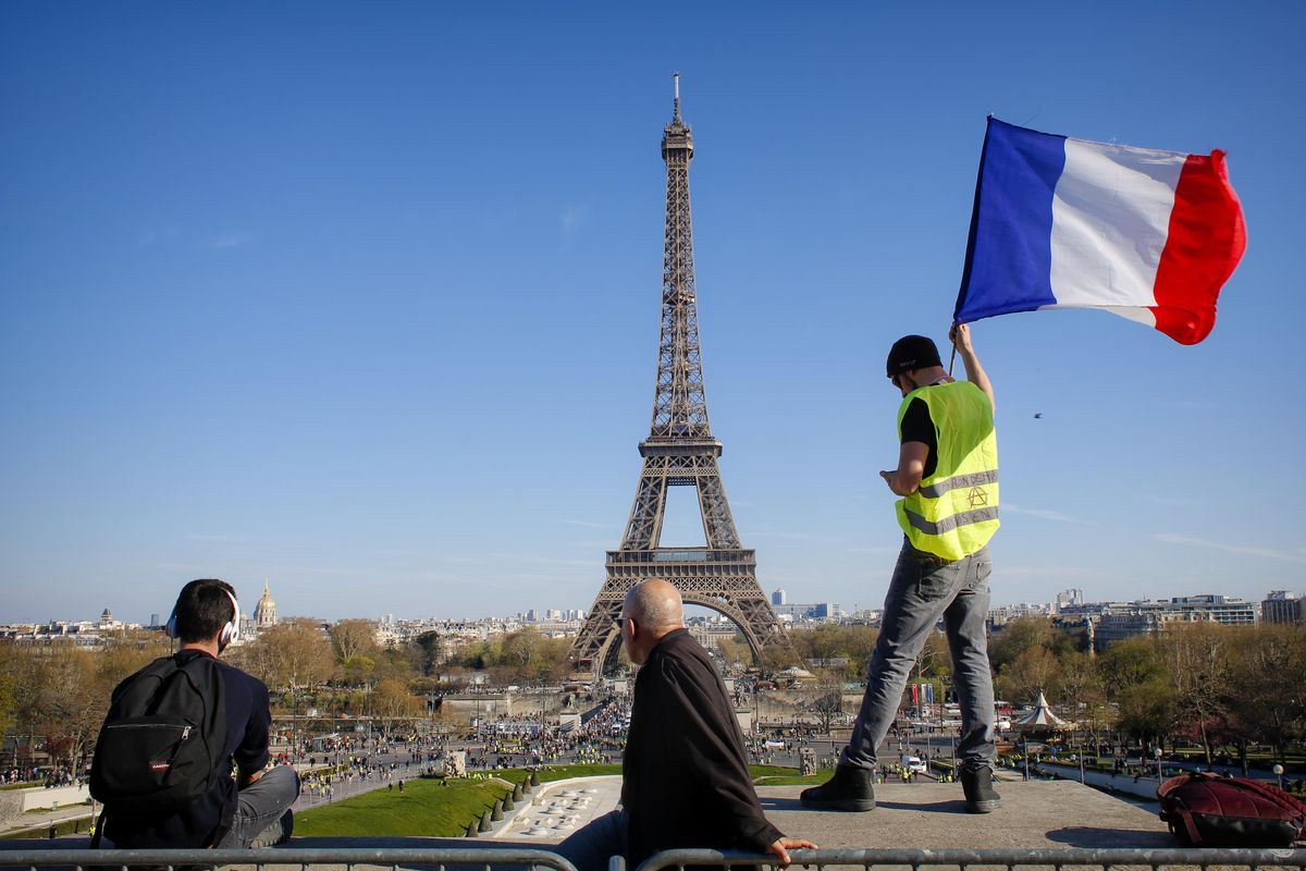 In this Saturday, March 30, 2019 photo, a man holds a French flag as French with the Eiffel Tower in the background, during protests in Paris. Paris is wishing the Eiffel Tower a happy birthday with an elaborate laser show retracing the monument