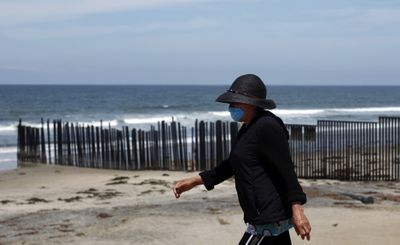 A woman wearing a mask as a precaution against the H1N1 virus walks on the beach near the U.S.-Mexico border wall in Tijuana, Mexico, on Sunday.  (Associated Press / The Spokesman-Review)