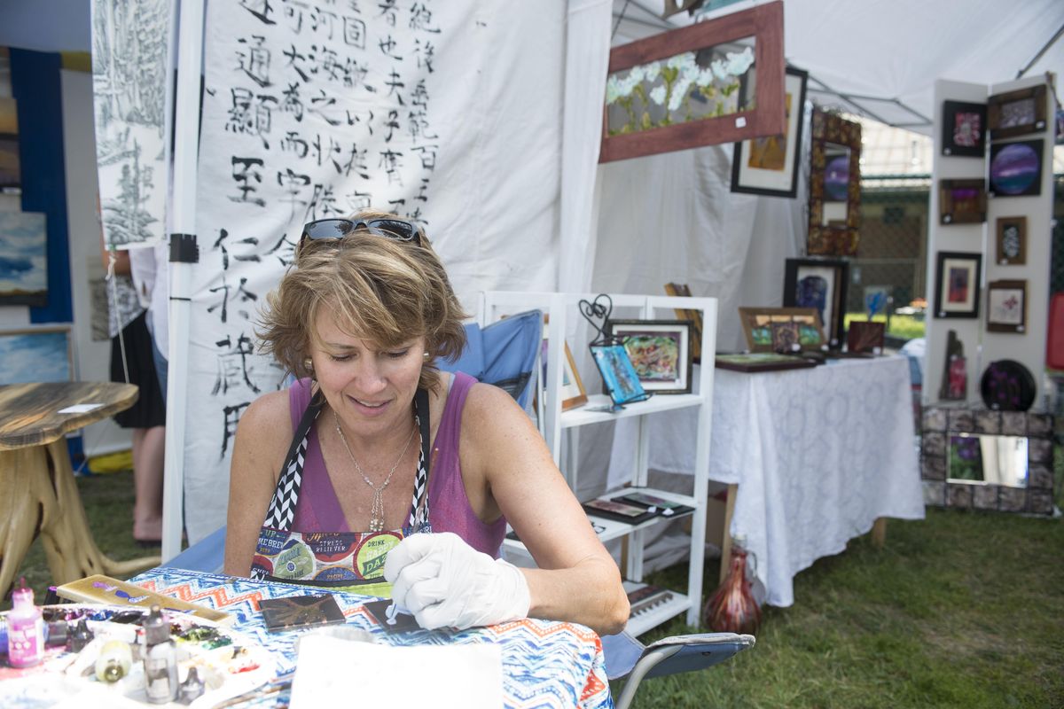 Artist Twyla-Lea Jensen paints on tiles using alcohol ink, a medium that will only stick to nonporous surfaces, Sunday, Aug. 6, 2017, at Art on the Green, the annual art festival on the grounds of North Idaho College. It was the first time at the festival for the Coeur d’Alene artist. (Jesse Tinsley / The Spokesman-Review)
