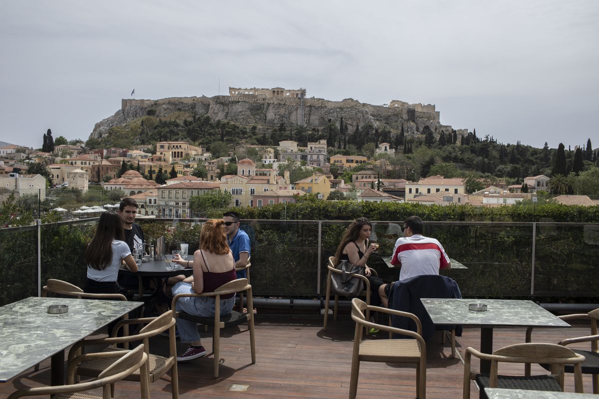 People sit in on a cafe terrace, in the Monastiraki district of Athens, with the ancient Acropolis hill in the background, Monday, May 3, 2021. Cafes and restaurants have reopened in Greece for sit-down service for the first time in nearly six months, as the country began easing coronavirus-related restrictions with a view to opening to the vital tourism industry in the summer.  (Petros Giannakouris)
