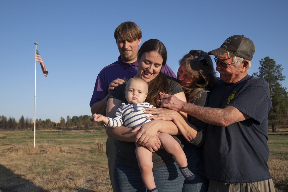 Nate and Bry Reynolds, with baby Tobias, stand with Nate’s parents, Malden fire Chief Dan Harwood and Tami Van Dyke, near the field where they waited out the Malden fire that burned down the Reynolds’ home on Labor Day 2020. The flag in the background is the same one that flew during the fire.  (JESSE TINSLEY)