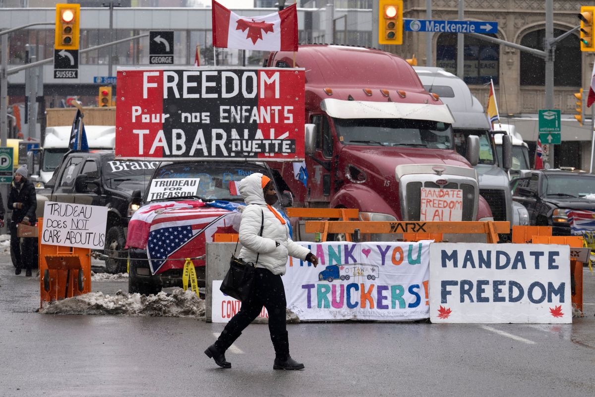 A woman crosses the street in front of vehicles parked as part of the trucker protest, Tuesday, Feb. 8, 2022 in Ottawa. Canadian lawmakers expressed increasing worry about protests over vaccine mandates other other COVID restrictions after the busiest border crossing between the U.S. and Canada became partially blocked.  (Adrian Wyld)