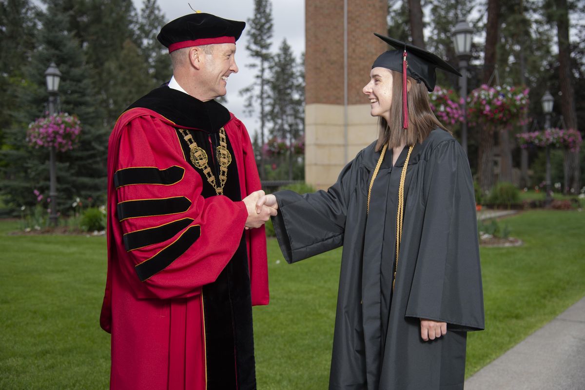 College graduate Lauren Taylor, 21, right, gets a graduation handshake from, her father, Whitworth University President Beck Taylor, right, Friday, May 15, 2020, at Whitworth University in north Spokane. Today would have been graduation day but the commencement ceremony has been postponed until October. Still, the Taylor family gathered for photos to celebrate Lauren’s graduation with double majors biophysics and chemistry. She plans to apply to medical school. Beck Taylor points out that she’s the only graduate this year who gets a handshake. (Jesse Tinsley / The Spokesman-Review)