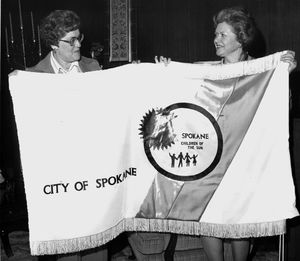 Mrs. W. Tom Mableson, left, and Mrs. Terry H. Tate display the new official city flag created by members of Spokane Falls Needlework Guild in March 1977. The flag, designed by Lloyd L. Carlson, who also created the Expo ’74 mobius strip symbol, replaced a 19-year-old lavender “Lilac City” flag.