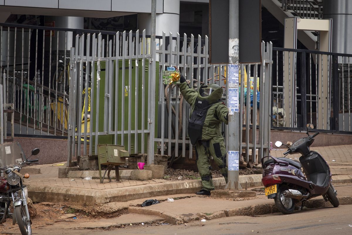A bomb disposal officer examines a suspicious package resembling a gift before subjecting it to a controlled explosion, next to the central police station in Kampala, Uganda, Tuesday, Nov. 16, 2021. Two loud explosions rocked Uganda