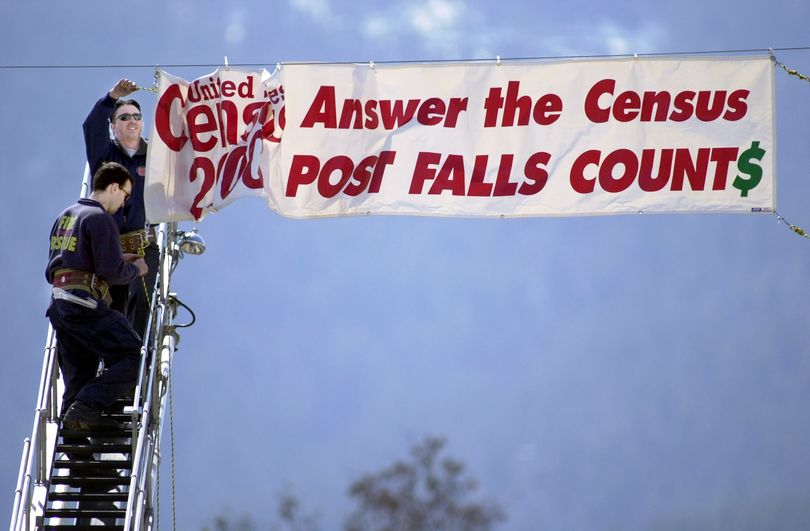 Post Falls firefighters Bryan Williams, top, and Kevin Amorebieta (cq) hang a banner Thursday morning reminding Post Falls residents to return their census forms.  The city received a $1000 