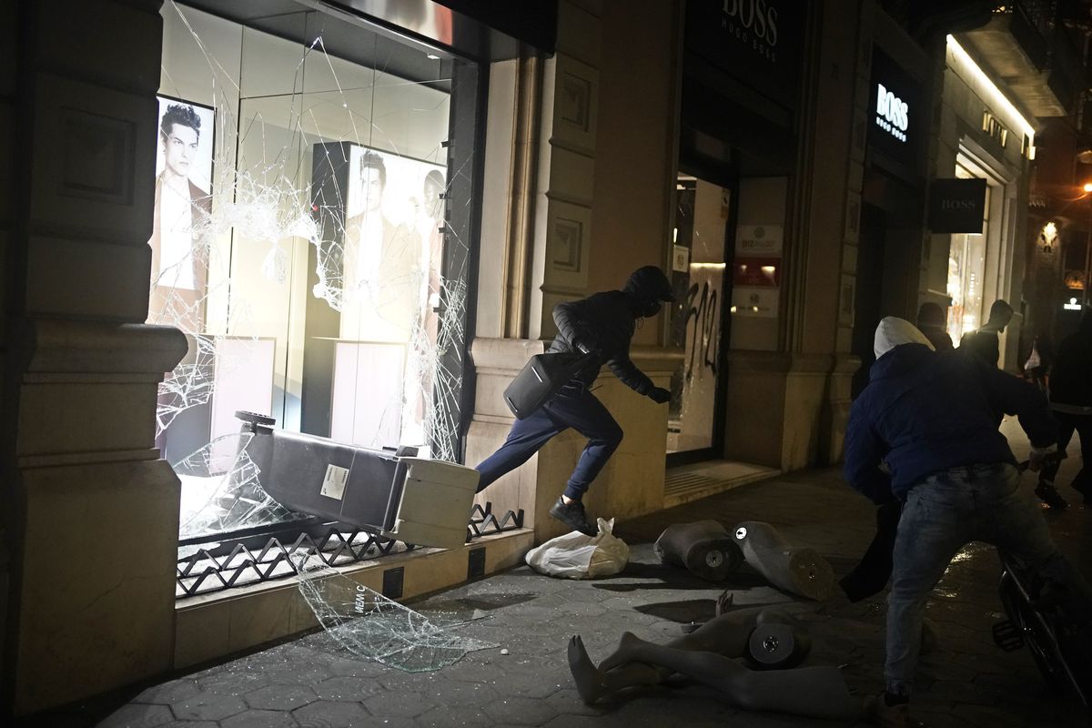 A person carrying goods runs from a smashed shop window during a protest condemning the arrest of rap singer Pablo Hasél in Barcelona, Spain, Saturday, Feb. 20, 2021. A fifth night of peaceful protests to denounce the imprisonment of a Spanish rap artist once more devolved into clashes between police and fringe group members who set up street barricades and smashed storefront windows in Barcelona.  (Joan Mateu)