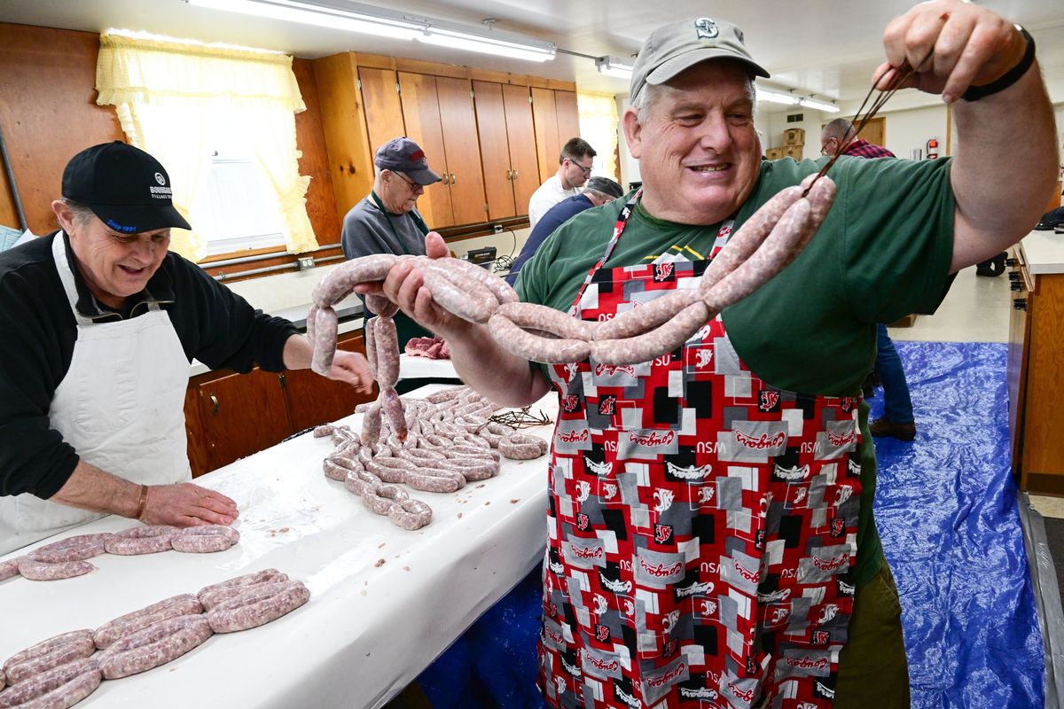 Ed Wolf, left, laughs as Tom Becker, right, hoists fresh sausage links from a preperation table to a storage box as the pair work with other volunteers on Thursday, March 2, 2023, to convert thousands of pounds of meat into sausage for Uniontown’s Sausage Feed to be held Sunday, March 5, from 10 am to 5 pm at the Uniontown Community Building in Uniontown, Wash.  (Tyler Tjomsland/The Spokesman-Review)