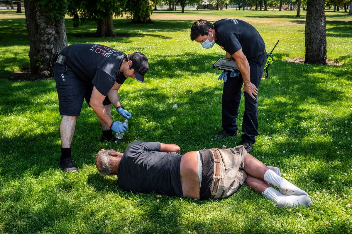 With temperatures well over 100 degrees on June 29, 2021, Spokane firefighter Sean Condon, left and Lt. Gabe Mills, assigned to the Alternative Response Unit of Station 1, check on the welfare of a man in Mission Park in Spokane.  (Colin Mulvany/The Spokesman-Review)