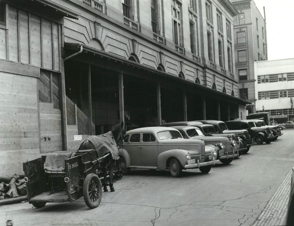 1941: One of the last two horse-drawn mail carts used by the Spokane Post Office for downtown mail delivery sits beside the original 1909 federal building on Riverside Court, a small side street used by postal delivery vehicles. The plaza in front of the 1967 Thomas S. Foley United States Courthouse next door was built up to level the sloping street. The 1941 expansion expanded post office space and also moved loading docks to the Main Avenue side. The light-colored three-story building at far right was the Cascade Building, which housed a variety of retail stores on the ground floor and a few apartments upstairs. It was torn down to clear the way for The Spokesman-Review building in the early 1980s.    (Spokesman-Review photo archives)