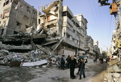 Palestinians walk in front of a building destroyed in an Israeli airstrike Saturday in Gaza City.  (Associated Press / The Spokesman-Review)