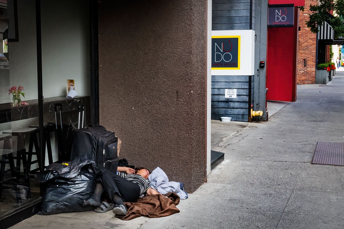 A woman sleeps on the sidewalk across from the Historic Davenport Hotel on West Sprague Avenue in September.  (Colin Mulvany/The Spokesman-Review)