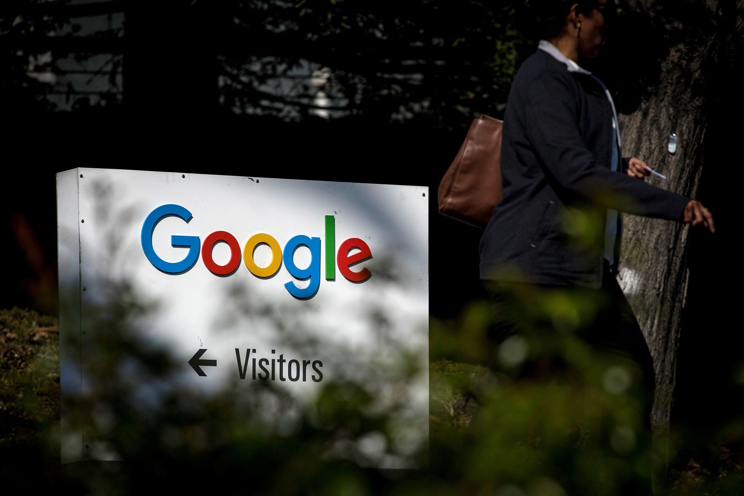 A photo of the google logo on a cement sign, with a person walking by to the right of the frame