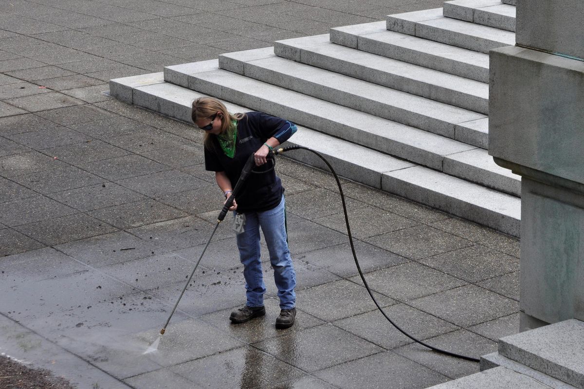 OLYMPIA – Megan McNealy, a state worker who spent much of last week cleaning graffiti off the steps of the Legislative Building, power washes the sidewalk Friday afternoon. (Jim Camden / The Spokesman-Review)