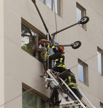 Firefighters use a ladder truck to reach two window washers left dangling from their safety lines on a six-story building after their platform apparently malfunctioned Thursday in Olympia. Olympia Fire Department personnel rescued the two men, one of whom was bleeding from the head. (Associated Press)