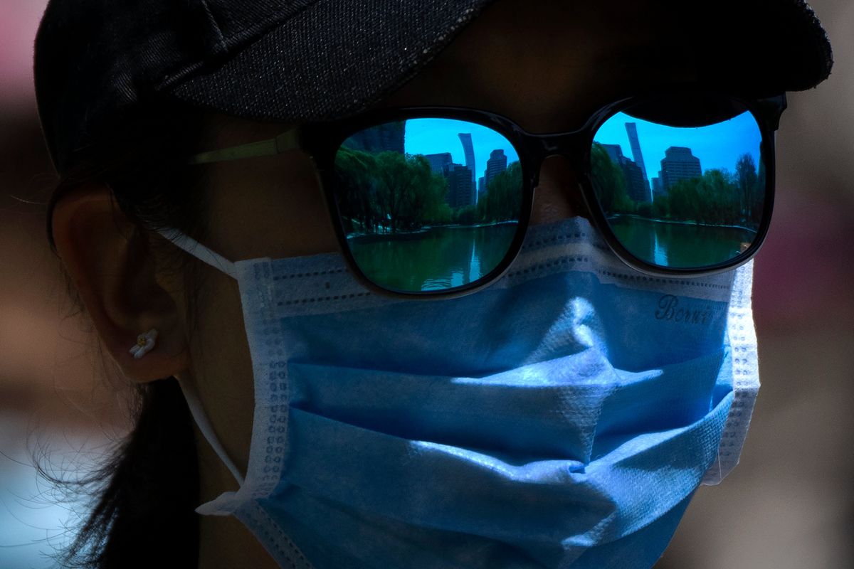 The skyline of Beijing is reflecting in the sunglasses of a woman wearing a face mask as she walks at a public park Thursday in Beijing.  (Associated Press)