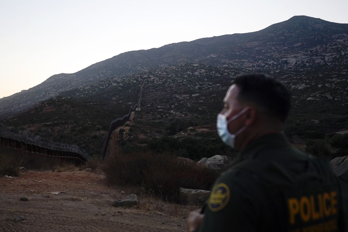 Border Patrol agent Justin Castrejon looks toward where the border wall makes its way over a mountain Thursday, Sept. 24, 2020, near Tecate, Calif. President Donald Trump’s reshaping of U.S. immigration policy may be most felt in his undoing of asylum. Castrejon says migrants pay $8,000 to $10,000 to be guided through the mountains and picked up by a driver once they reach a road.  (Gregory Bull)