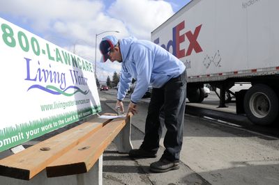 John Ralph, who works for a small outdoor advertising company,  staples a message to a bench Wednesday, telling users about the city’s plan to remove all the benches put up and maintained by advertising companies.  (Jesse Tinsley / The Spokesman-Review)