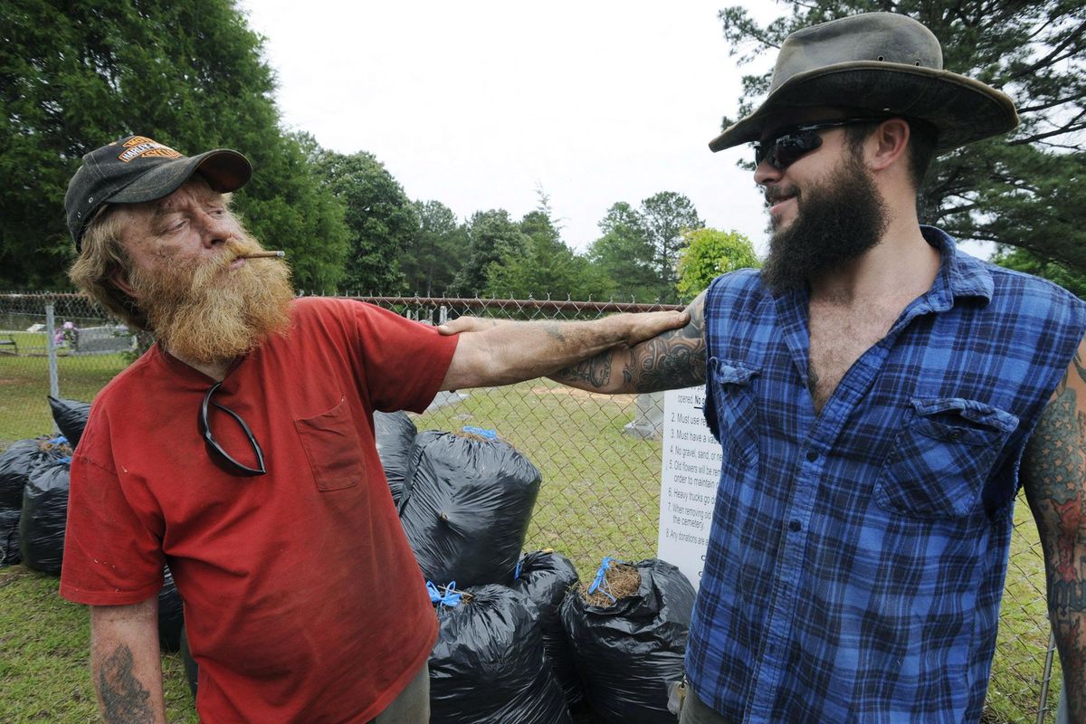In this Wednesday, May 3, 2017 photo,  Jimmy Frank Hicks, left, and nephew Tyler Goodson of the hit podcast "S-Town" stand at the grave of friend John B. McLemore, who is also featured in the serialized show. Dimes, rocks and trinkets have started showing up on McLemore