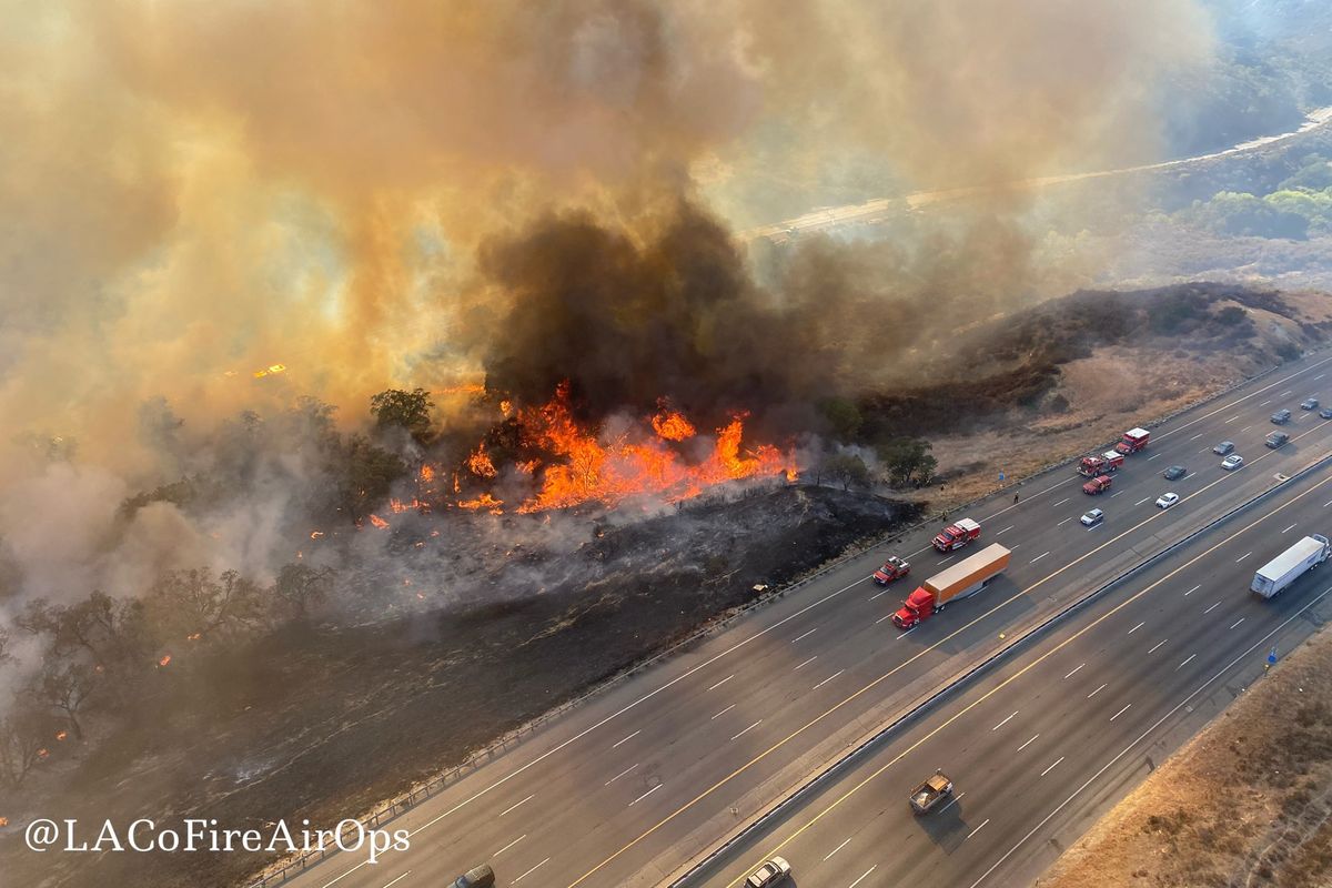 In this aerial photo released by the Los Angeles County Fire Department Air Operations traffic passes the Route fire, a brush wildfire off Interstate 5 north of Castaic, Calif., on Saturday, Sept. 11, 2021.  (HOGP)