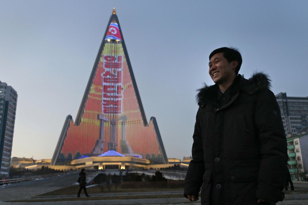 In this Dec. 20, 2018, photo, light designer Kim Yong Il smiles during an interview with the Associated Press as his creation, the light show displaying propaganda messages on the facade of the pyramid-shaped Ryugyong Hotel, is seen in the background in Pyongyang, North Korea. For several hours each night, the building that doesn
