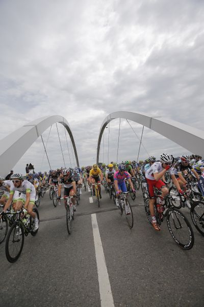 A pack of riders at the Tour de France pass a bridge spanning the Meuse river during the start of the second stage in Belgium. (Associated Press)