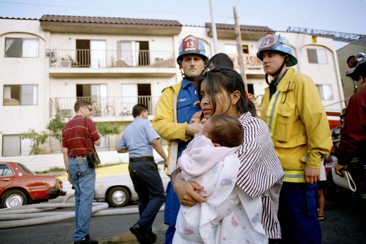 In this May 3, 1993, file photo, May Isabela Diego holds her infant son Pedro in the aftermath of a fire in an apartment complex in the Westlake section of Los Angeles. Diego had to drop her two children out of a window as fire threatened their safety. (Michael Tweed / Associated Press)