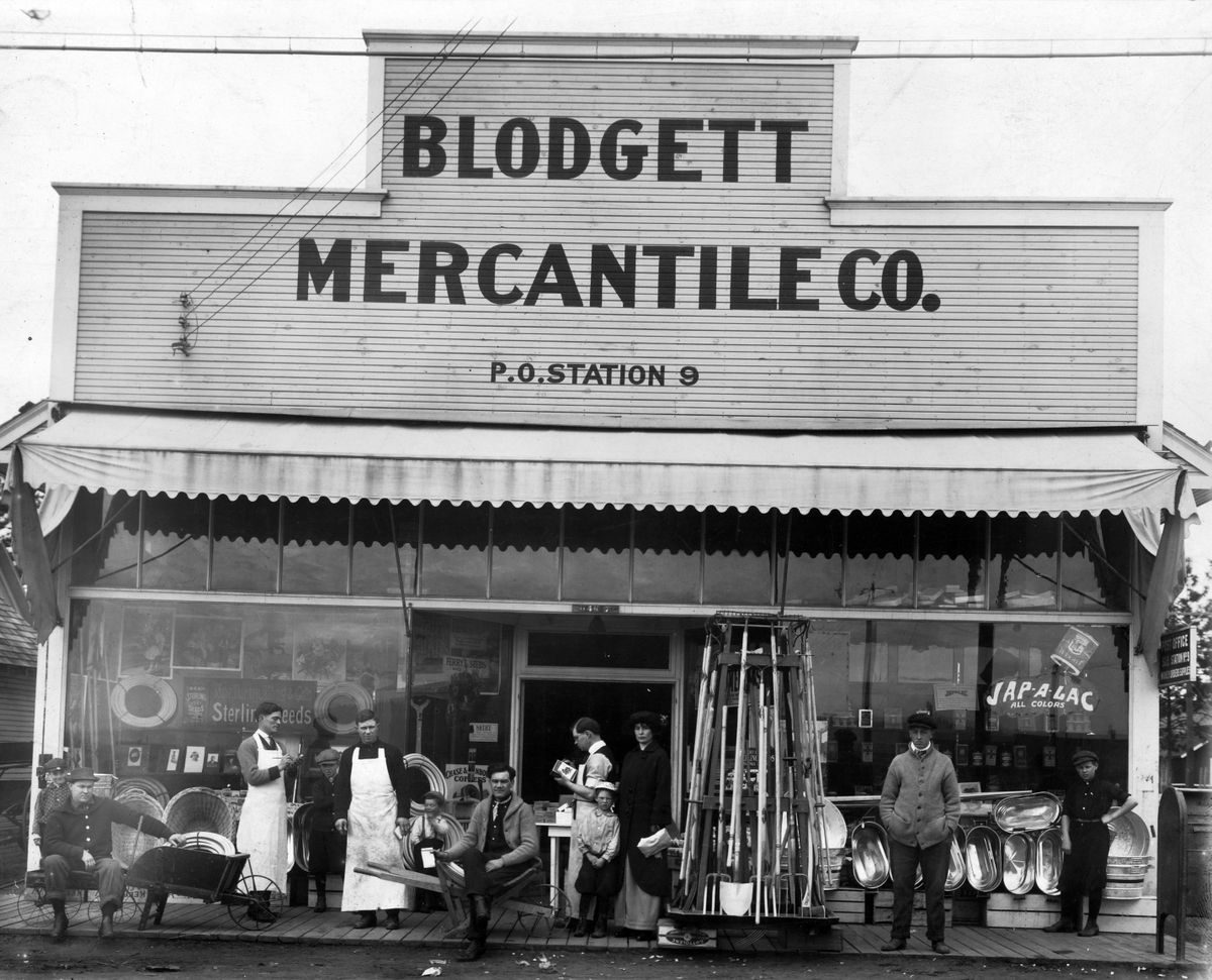 1915: Blodgett Mercantile caters to customers at the corner of Nevada and Wellesley. Pictured are, from left: unidentified man with wheelbarrow, Lee Bryant (apron), Charley Dole (apron), Lovell “Bump” Blodgett (child); Lovell Blodgett, C.A. Blodgett (reading book), James Blodgett (child), Emma Blodgett and two unidentified customers.