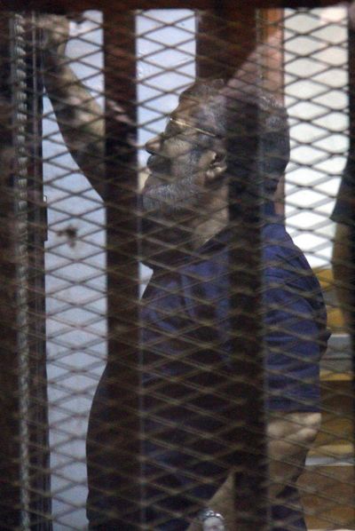 Ousted Egyptian President Mohammed Morsi waves Saturday from inside a cage in a makeshift courtroom in the national police academy in eastern Cairo. (Associated Press)
