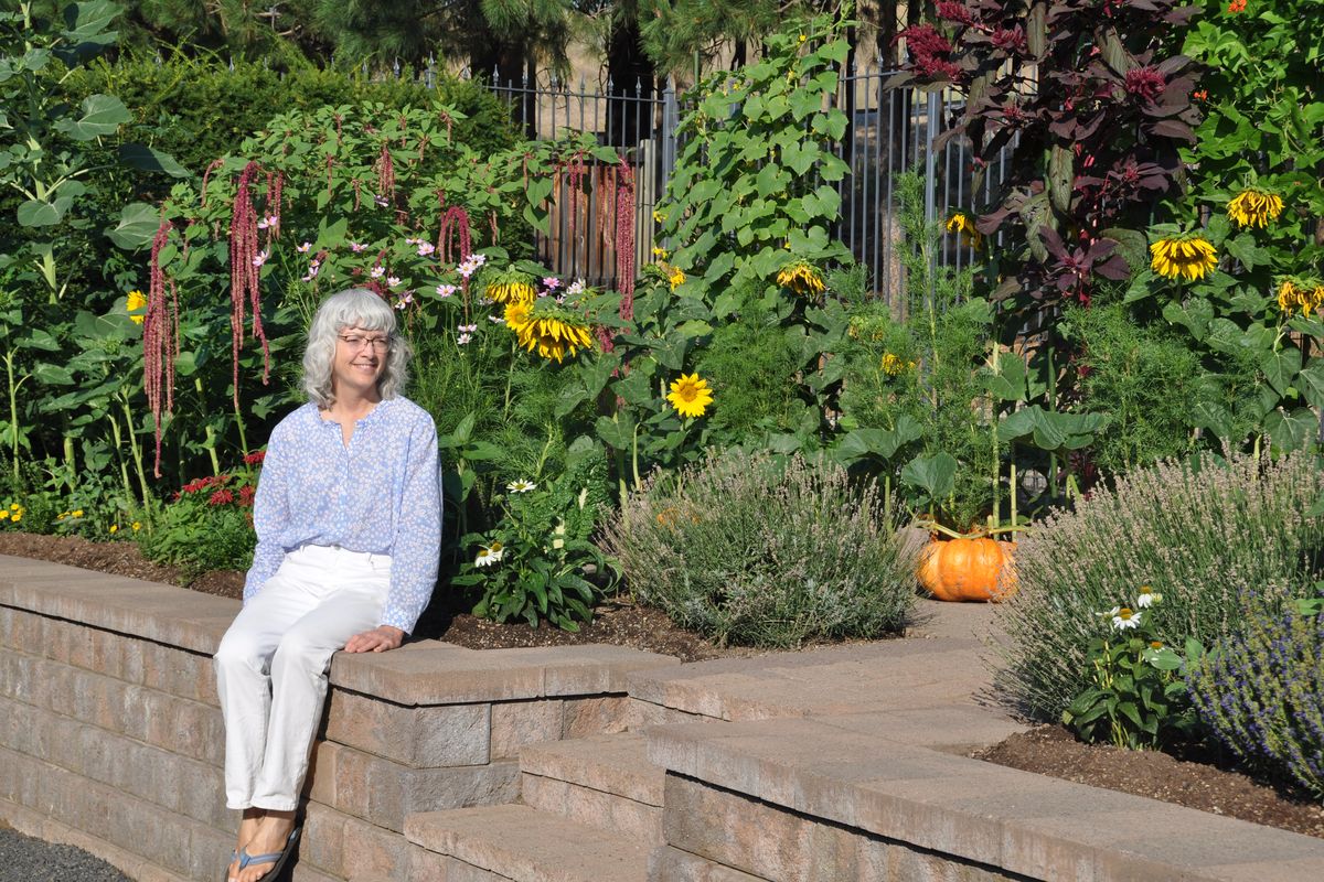 Patty Sparks sits next to her terraced Spanish-style vegetable garden backed by sunflowers, lavender, Love-Lies-Bleeding amaranth and a large Cinderella pumpkin that will be made into pies.  (Pat Munts/For The Spokesman-Review)