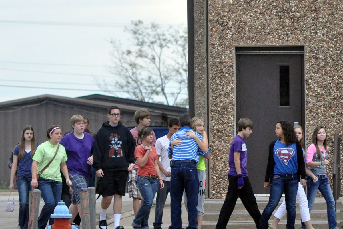 A Stillwater Junior High student hugs a member of the staff as her class is escorted to a waiting bus following the death of a student Wednesday, Sept. 26, 2012 in Stillwater, Okla. A 13-year-old student shot and killed himself in a hallway at an Oklahoma junior high school before classes began Wednesday, police said, terrifying teenagers who feared a gunman was on the loose. (Chase Rheam / Stillwater News Press)