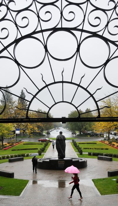 Walkers in the rain pass the St. Ignatius of Loyola statue on the Gonzaga University campus on Thursday. (Dan Pelle)