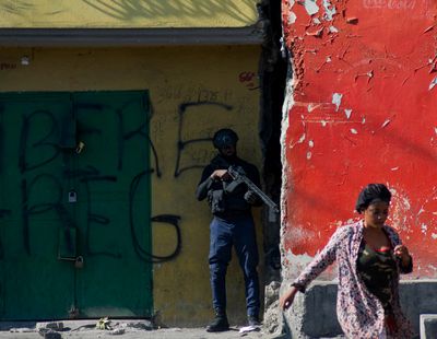 A woman walks past an armed police officer monitoring a street after gang violence the previous night, on March 22, 2024, in Port-au-Prince, Haiti. (Clarens Siffroy/AFP/Getty Images/TNS)  (Clarens Siffroy/AFP/Getty Images North America/TNS)