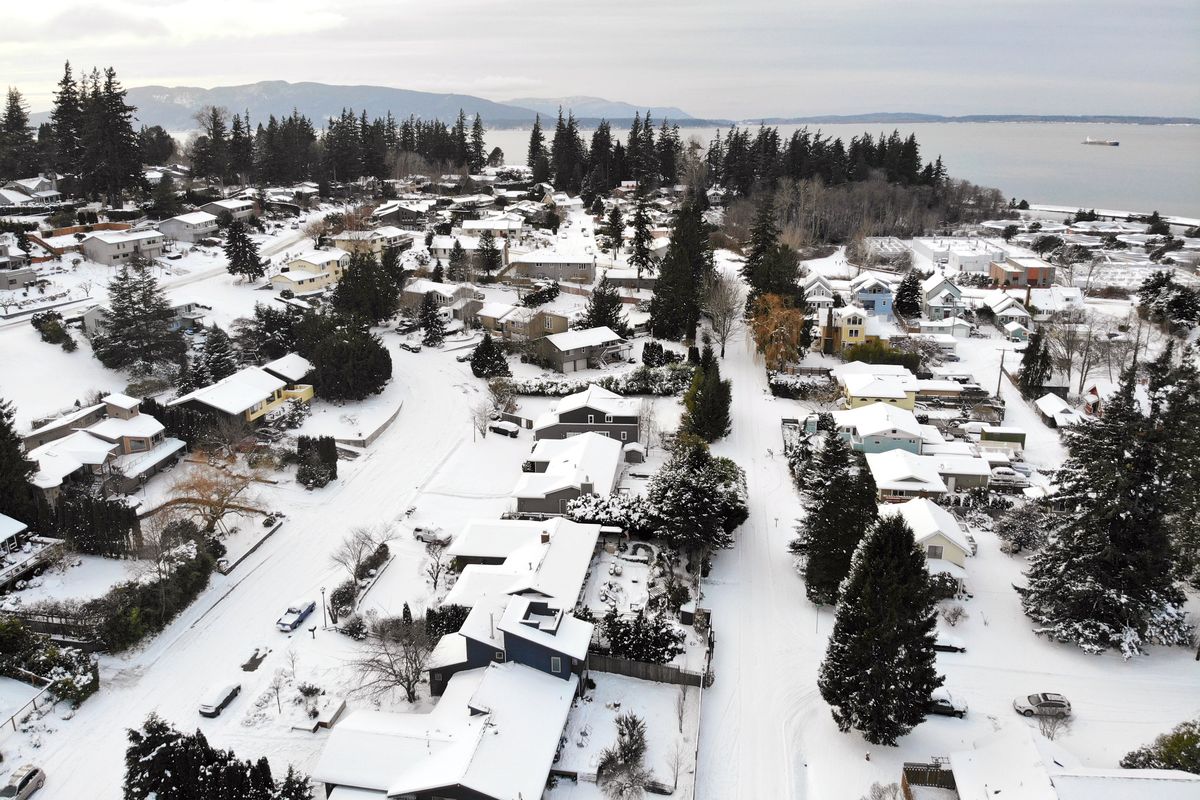 In this photo taken from a drone, snow covers streets, sidewalks and homes where nearly a foot of snow fell over the weekend, Monday, Dec. 27, 2021, in a neighborhood near Bellingham Bay in Bellingham, Wash. Emergency warming shelters were opened throughout western Washington and Oregon as temperatures plunged into the teens and forecasters said an arctic blast would last for several days.  (Elaine Thompson)