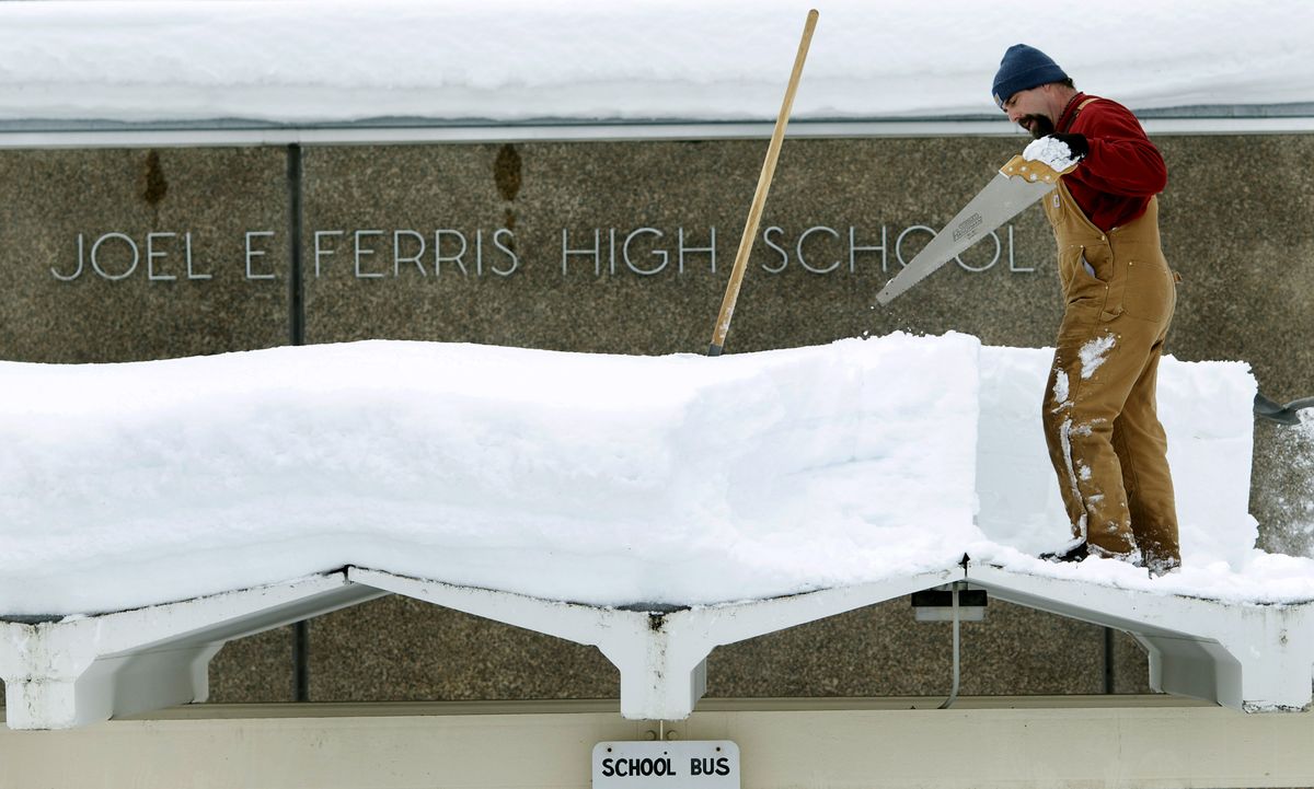 Norm Carveth, of the Spokane Public Schools maintenance department, uses a saw to cut snow into shovel-size chunks as he helps clear the roof of the bus loading area at Ferris High School in Spokane on Monday. Crews were clearing roofs and lots at the district’s 54 schools. (Colin Mulvany / The Spokesman-Review)