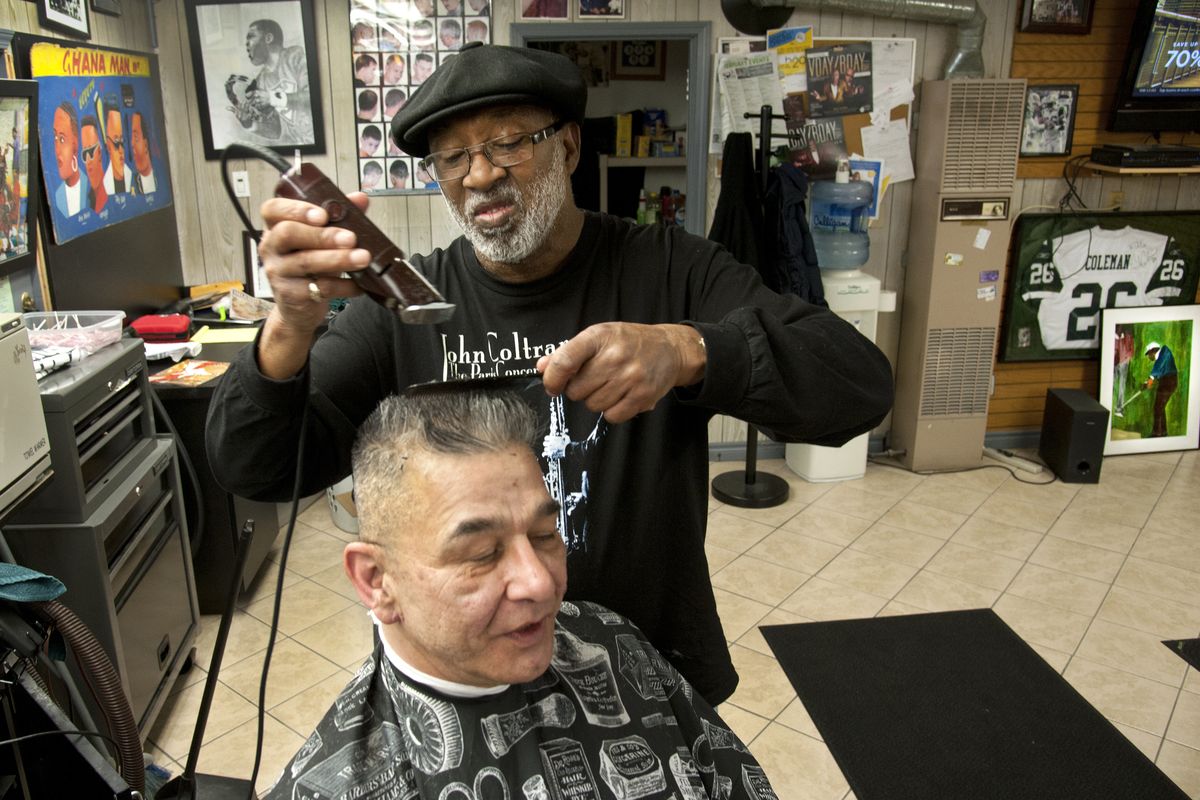 Larry Roseman cuts John McCormack’s hair at Larry’s Barber and Styling Shop. A painting of Charlie Sifford sits on floor at far right. (Dan Pelle)