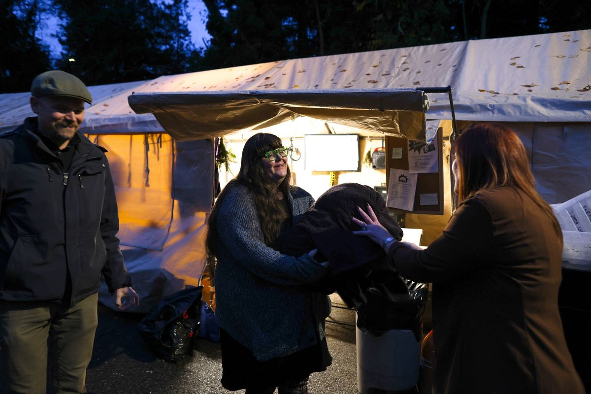 Cydney Moore, center, and Daniel Martin, left, both from the Burien Community Support Coalition, recieve blankets and clothing from Linda Clark, right, a Burien resident, at Sunnydale Village, a homeless encampment behind the Oasis Home Church in Burien, Washington, on Thursday, Dec. 14, 2023. Clark has also donated an iron, towels, washcloths, a ten man tent, blankets and comforters in the past. “I think this is amazing,” she says.    (Karen Ducey/The Seattle Times/TNS)