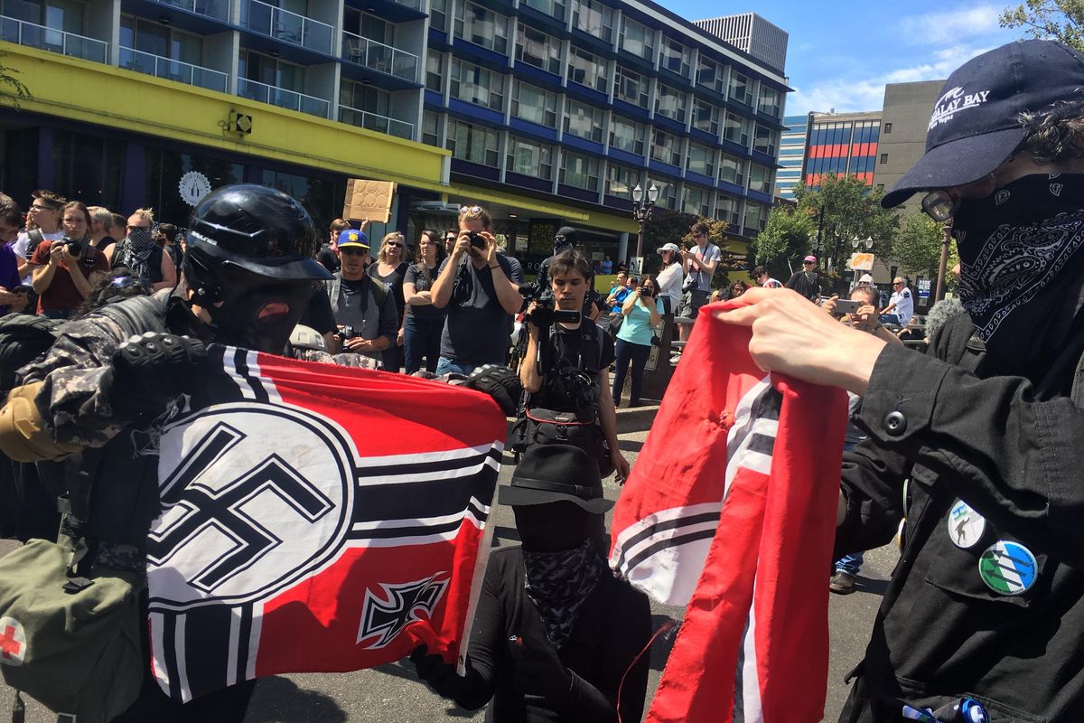 Counter protesters tear a Nazi flag, Saturday, Aug. 4, 2018 in Portland. Small scuffles broke out Saturday as police in  deployed “flash bang” devices and other means to disperse hundreds of right-wing and self-described anti-fascist protesters. (Manuel Valdes / Associated Press)