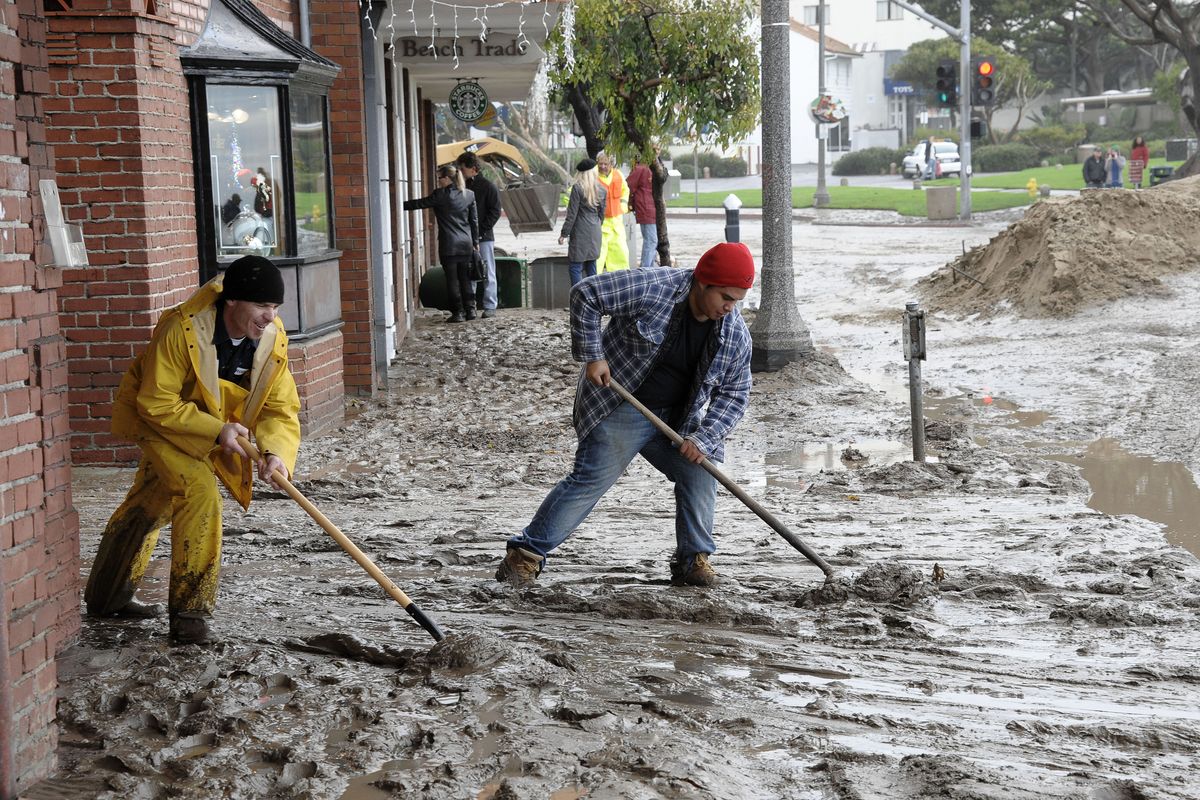 Workers shovel mud out onto the Pacific Coast Highway from the entrance to the Laguna Cinemas in Laguna Beach, Calif., on Wednesday.  (Associated Press)