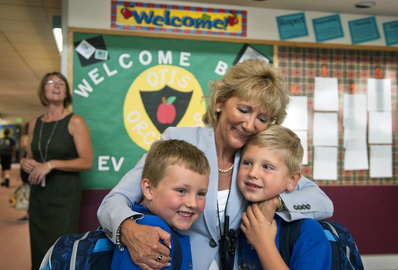 Otis Orchards School principal Suzanne Savall hugs cousins Devon Nelson, 7,left, and Zachary Hughes, 7, as they return for second grade on the first day of school Thursday. Kindergarten teacher Stacey Brinkley awaits arrivals at left. (Dan Pelle)