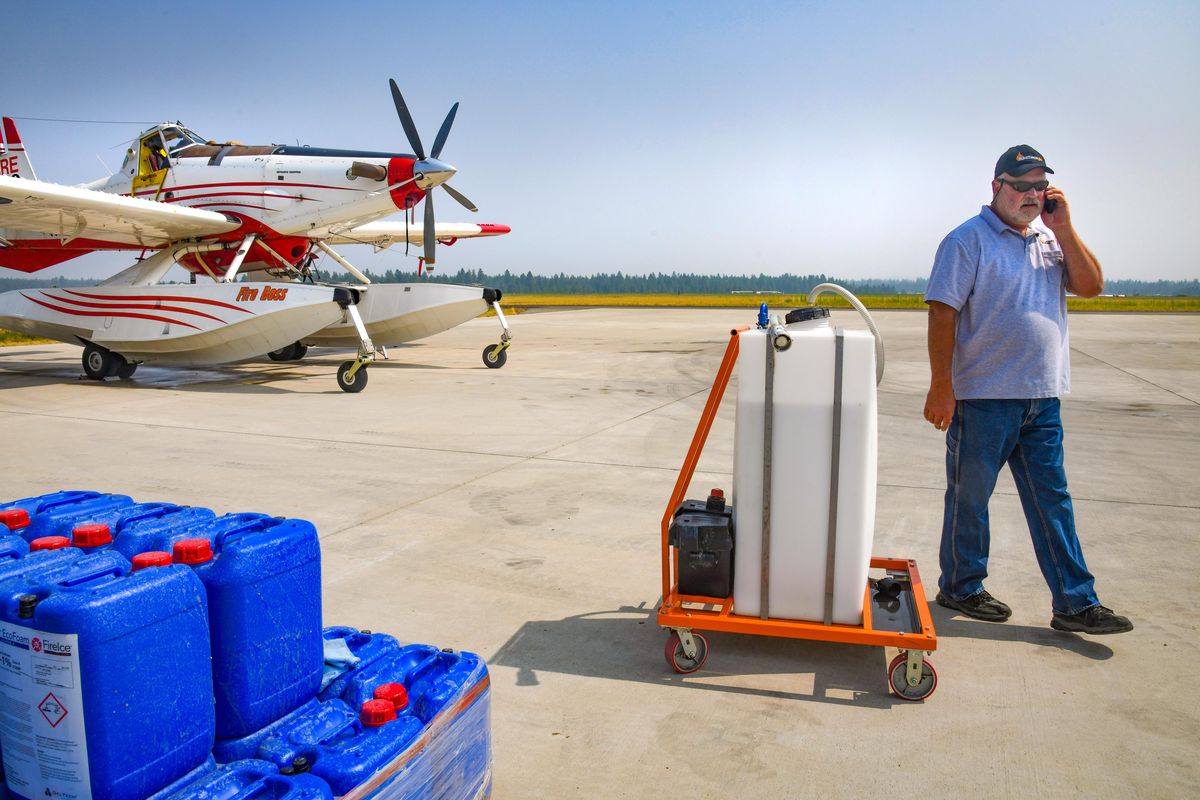 Harlan Johnson, V.P and G.M of G5 BioSolutions, takes a phone call from his boss while near a Fire Boss aircraft at Deer Park Airport, Wednesday, Aug. 15, 2018. The blue containers, at left, hold the fire suppressant BlazeTamer380. The solution is added to the white tank, at center, and then rolled out loaded into the water tanks aboard the firefighting plane. Blazetamer380 enhances the water to better efficiency in fighting Class A fires. (Dan Pelle / The Spokesman-Review)