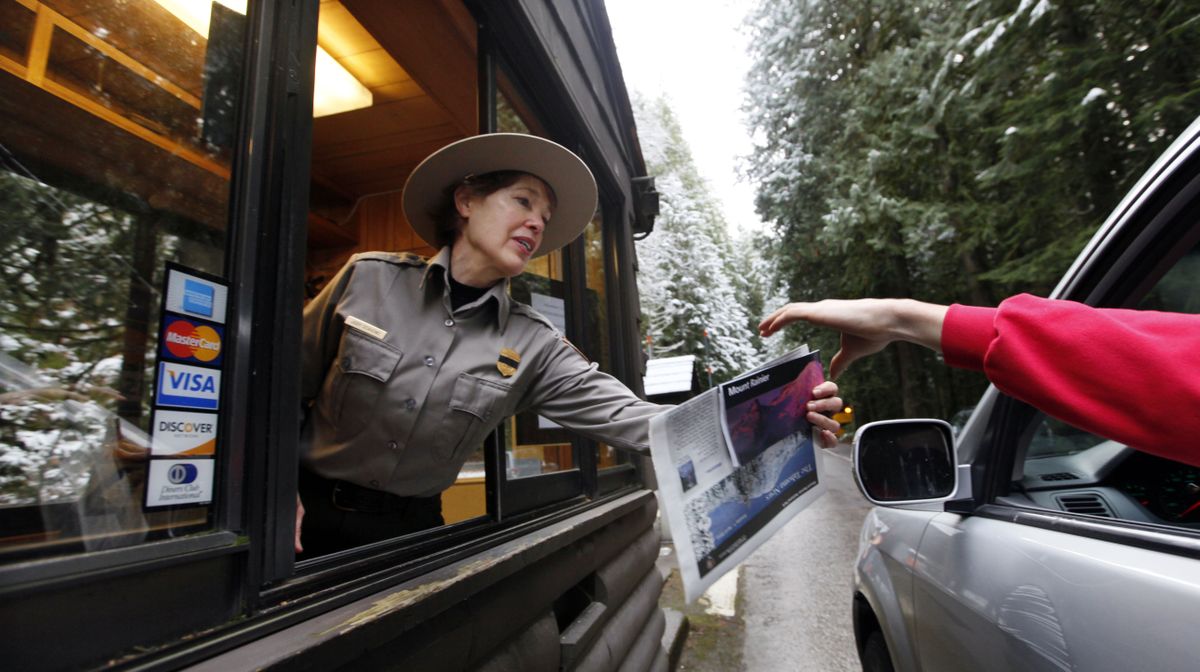 Ranger Judy Scavone, with a black band across her badge, hands park information to a visitor Saturday morning. (Associated Press)