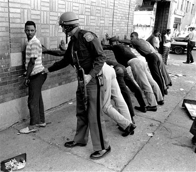 In this July 24, 1967 file photo, a Michigan State police officer searches a youth on Detroit's 12th Street where looting was still in progress after the previous day's rioting. (Associated Press)