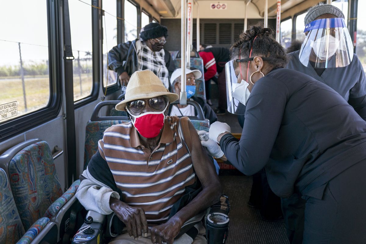 A senior receives a COVID-19 vaccine from a healthcare worker on Feb. 3 after arriving on a bus to a vaccination site at Anquan Boldin Stadium in Pahokee, Fla. (Greg Lovett)