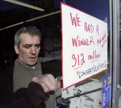 Steve Gallucci hangs a sign at Coulson’s News Center in Albany, N.Y., where the winning Mega Millions ticket was sold. (Associated Press)