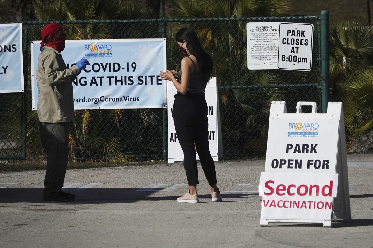 In this Jan. 27, 2021 photo, woman asks directions at the entrance to Vista View Park where a COVID-19 vaccination site has opened for second doses in Davie, Fla. As health officials race to vaccinate people across the U.S., the need to give each person two doses a few weeks apart is adding a layer of complexity to the country’s biggest-ever vaccination campaign.  (Joe Cavaretta)